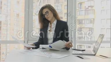 办公室工作人员，戴眼镜的女商人坐在办公室的扶手椅上，在办公室里检查文件和写作任务
